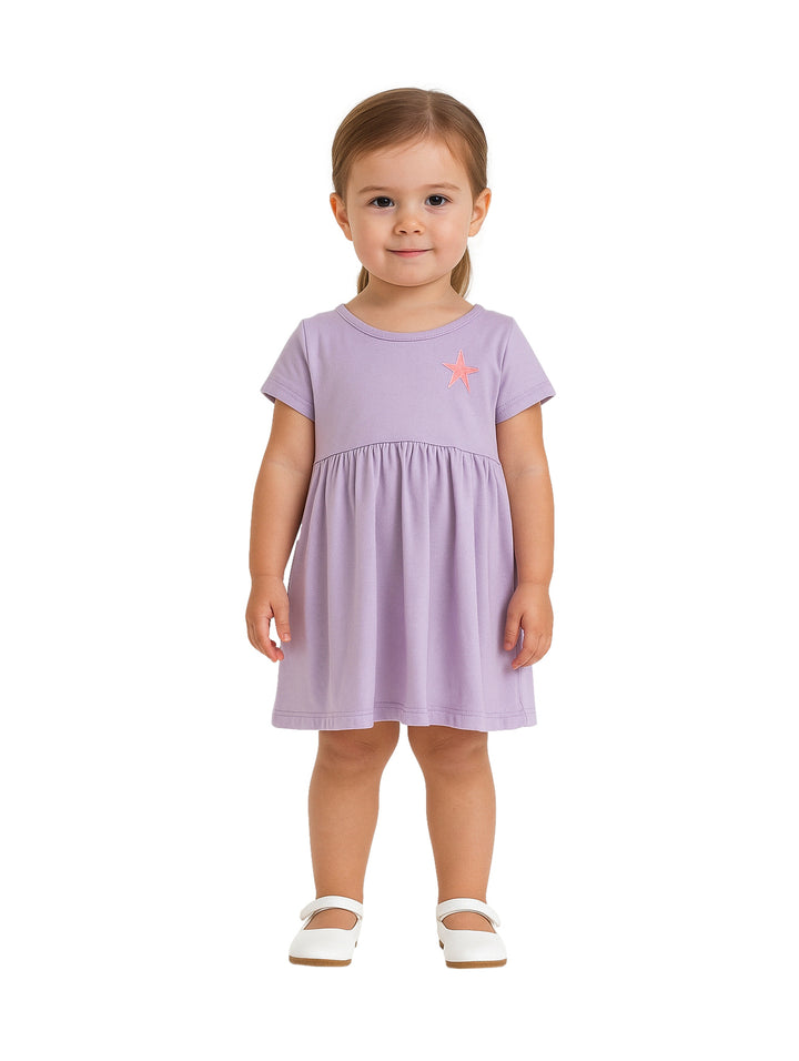 Niña con vestido corto color lila y detalle de estrella rosa en el pecho.