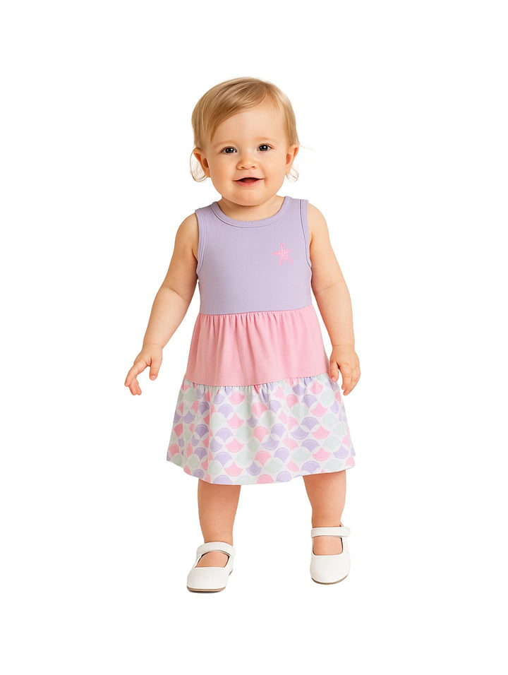 Niña pequeña con vestido casual en tonos lila y rosa con estampado de escamas en el borde inferior.