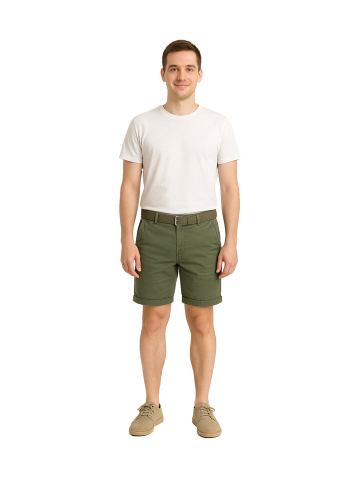 Hombre modelando bermudas color verde militar con playera blanca y zapatos beige sobre fondo blanco.