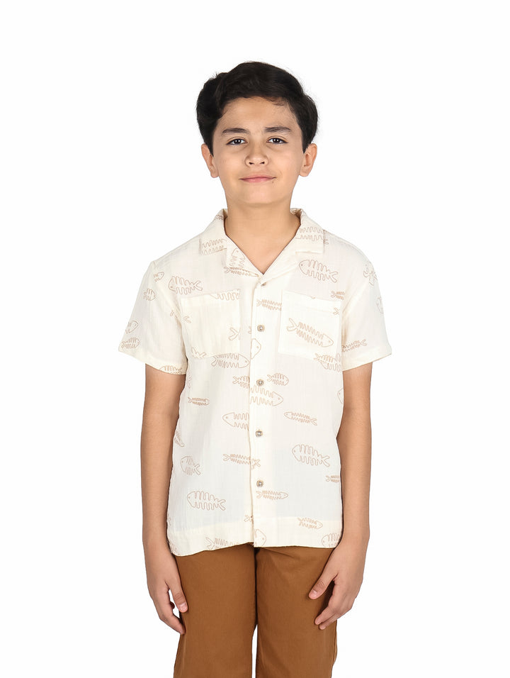 Niño vistiendo una camisa de manga corta color beige claro con estampado de peces.