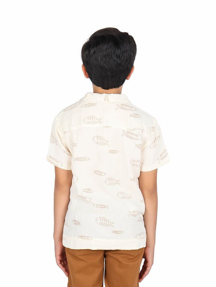 Niño vistiendo una camisa de manga corta color beige claro con estampado de peces.