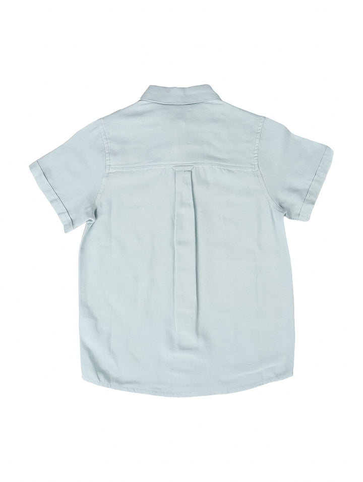 Camisa de lino color azul claro para niño, con manga corta y cierre frontal de botones.