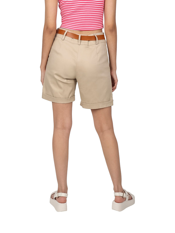 Mujer vistiendo bermudas color beige con cinturón café y sandalias blancas sobre fondo blanco.