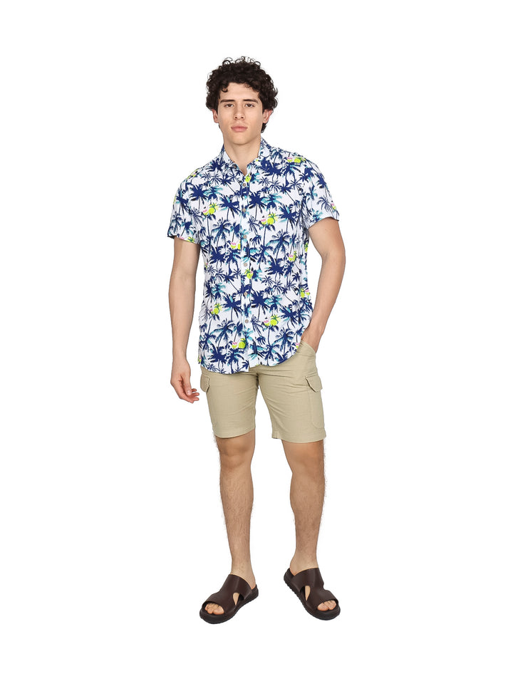 Hombre vistiendo camisa hawaiana blanca con estampado de palmeras azules y verdes.
