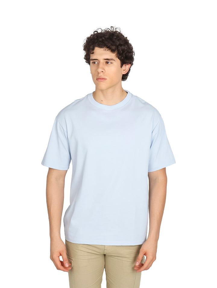 Hombre vistiendo una playera oversize de color azul claro con cuello redondo y manga corta.