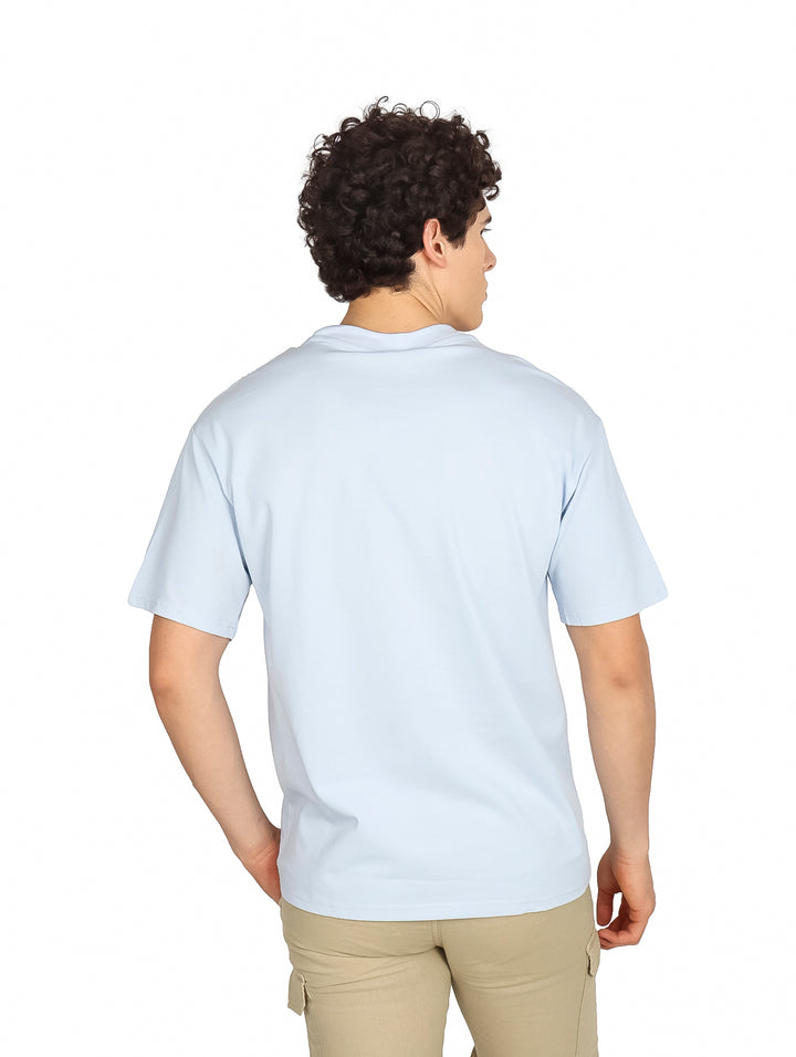 Hombre vistiendo una playera oversize de color azul claro con cuello redondo y manga corta.