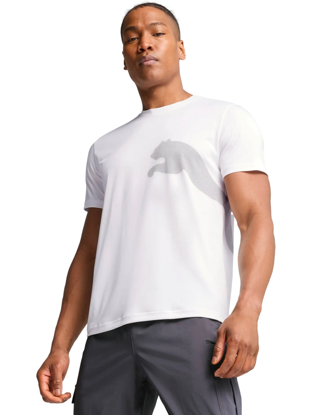 Hombre vistiendo playera blanca PUMA de manga corta con logotipo grande en el pecho y pantalones deportivos grises.