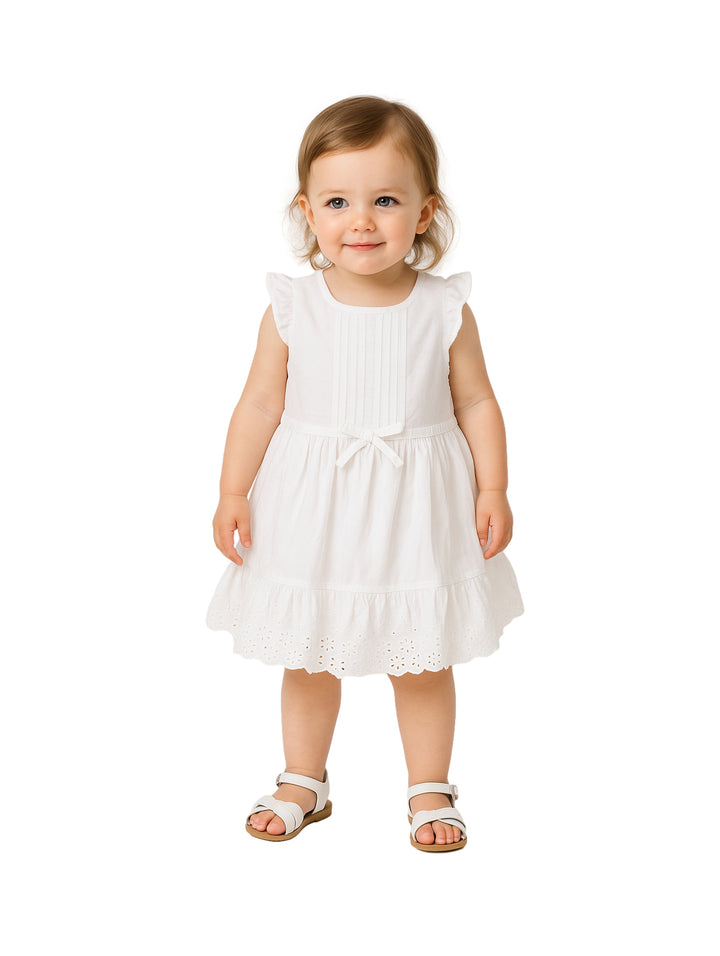 Niña pequeña vistiendo un vestido blanco sin mangas con moño en la cintura y detalles de encaje en el borde inferior.