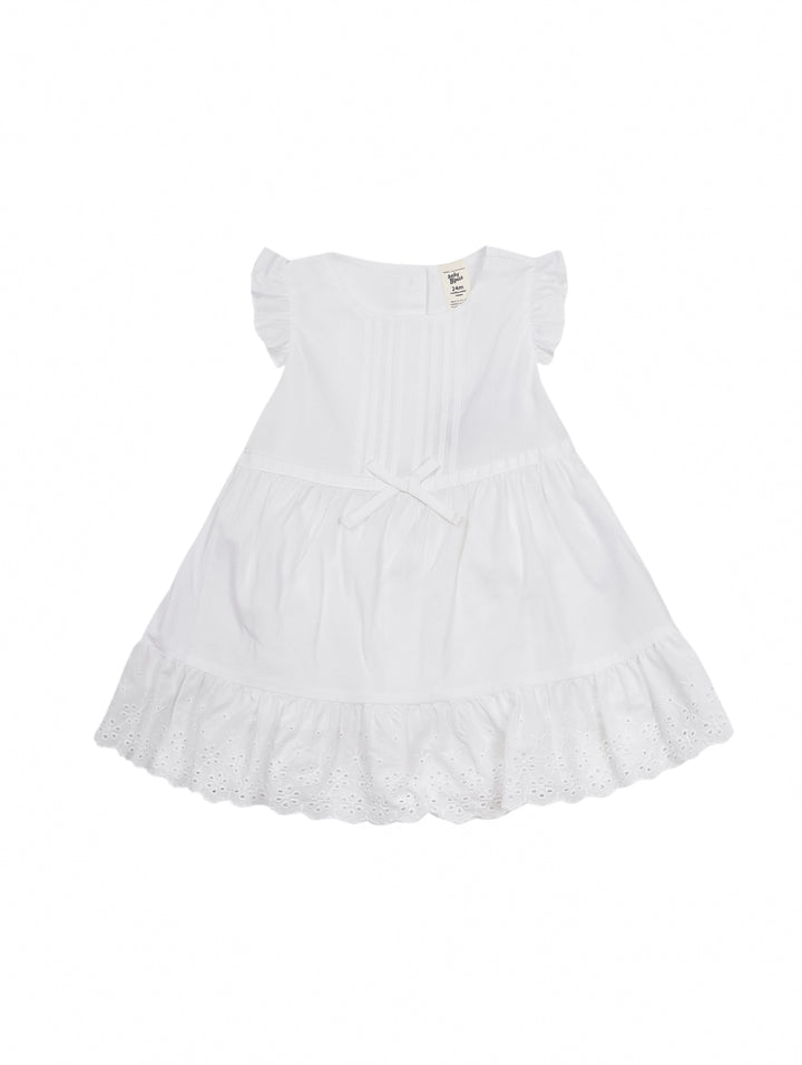 Niña pequeña vistiendo un vestido blanco sin mangas con moño en la cintura y detalles de encaje en el borde inferior.