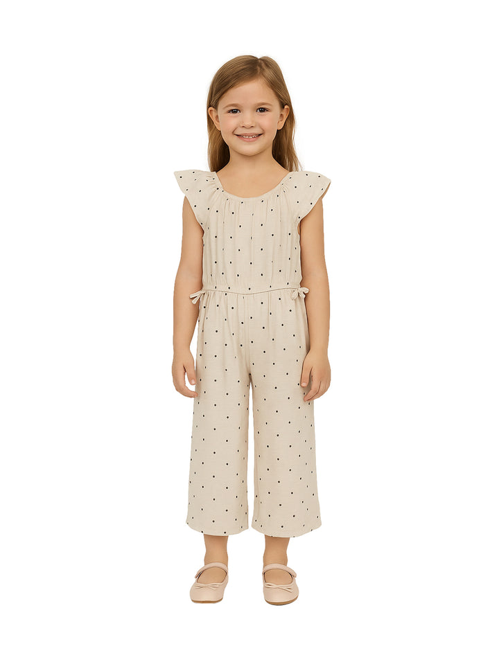 Niña vistiendo un mono beige con pequeños lunares negros y zapatos a juego.