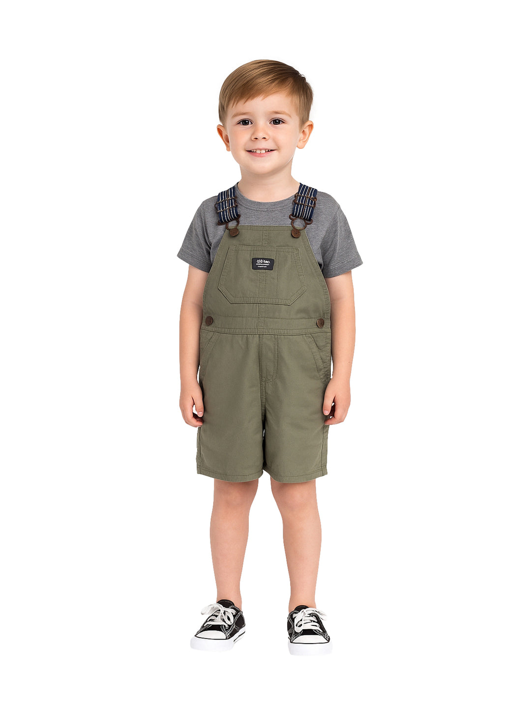Niño vistiendo un overol corto color olivo con tirantes y una camiseta gris.