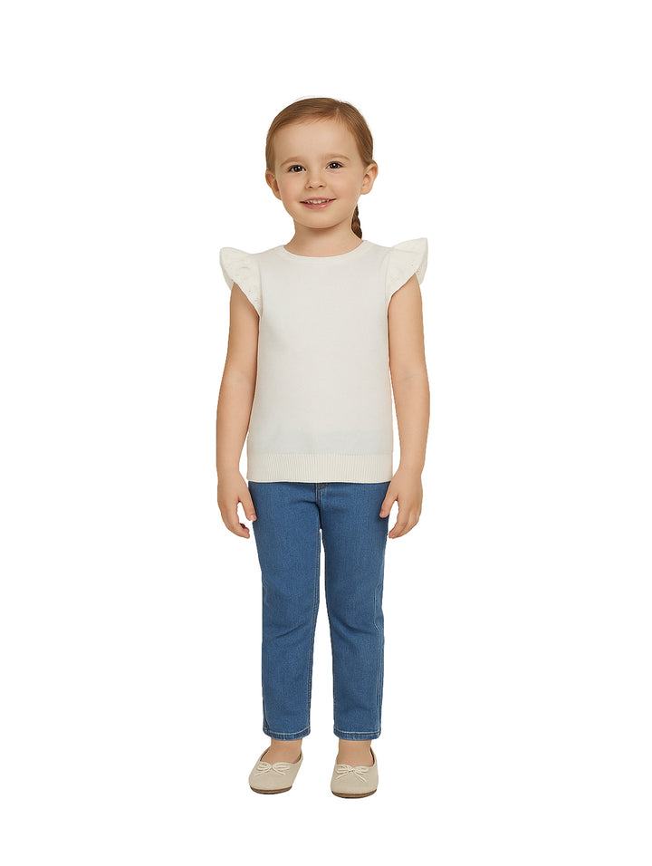 Niña vistiendo una blusa blanca de manga corta con volantes y pantalones azules.
