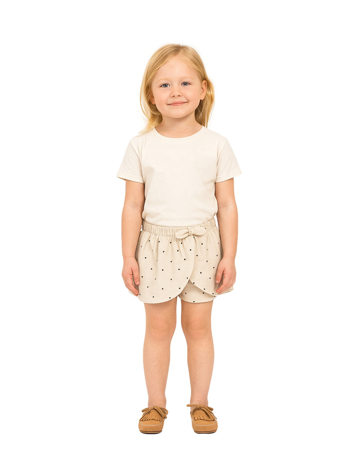 Niña vistiendo un short falda color beige con lunares oscuros y un lazo en la cintura.