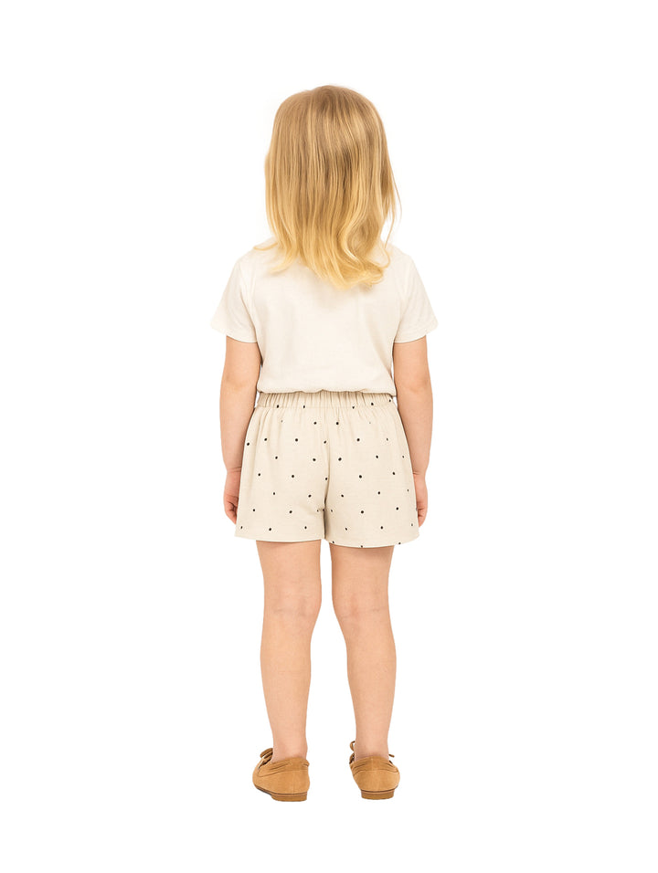 Niña vistiendo un short falda color beige con lunares oscuros y un lazo en la cintura.