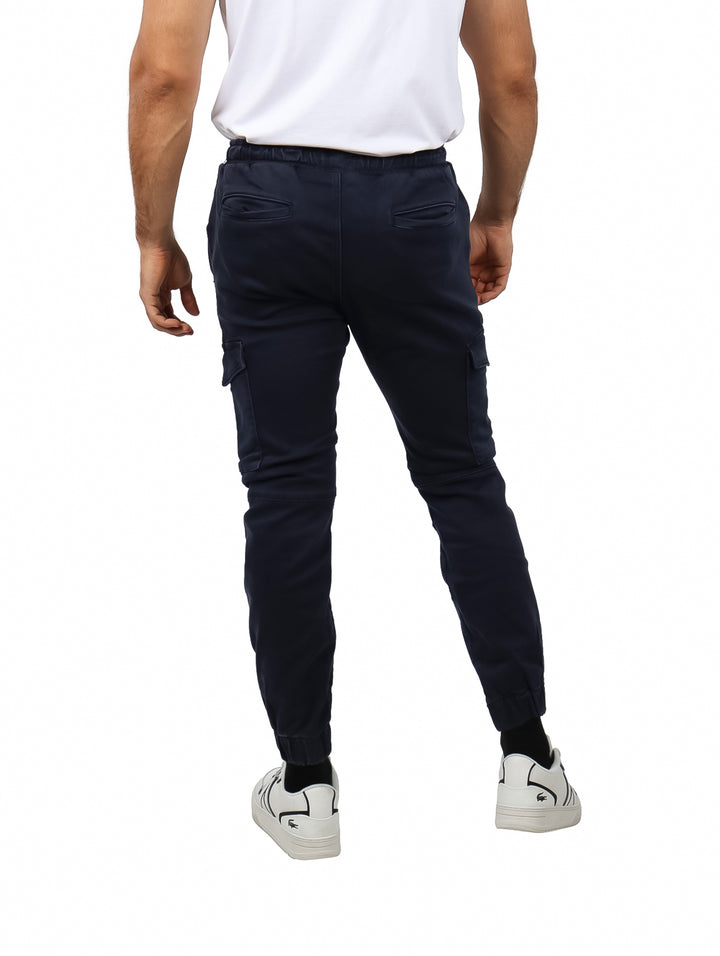 Hombre vistiendo pantalones jogger color azul marino con bolsillos laterales y calzado blanco.
