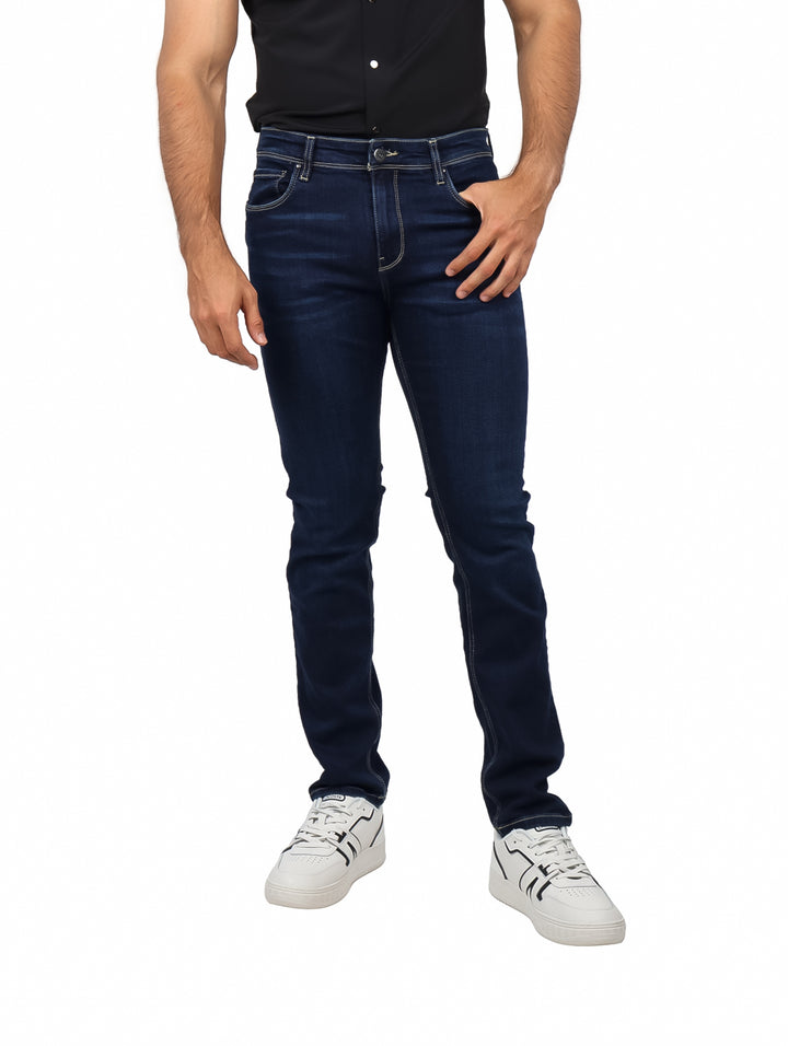Hombre vistiendo pantalones jeans de color azul marino oscuro con corte ajustado y calzado blanco.