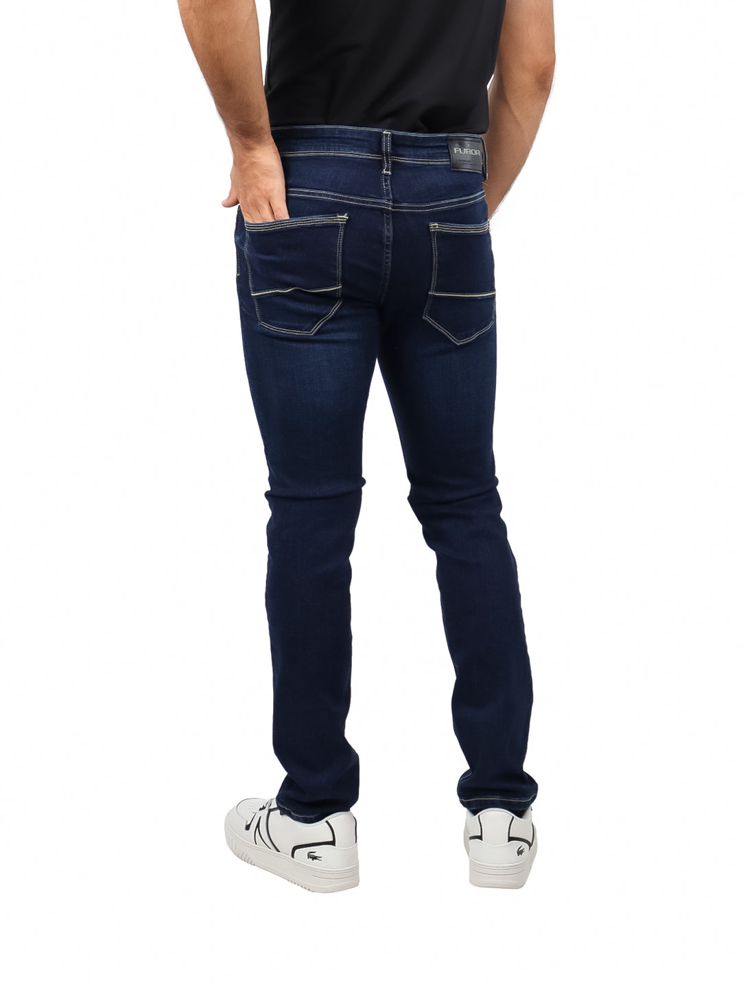 Hombre vistiendo pantalones jeans de color azul marino oscuro con corte ajustado y calzado blanco.