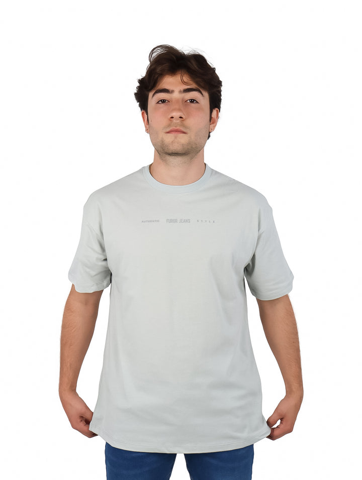Hombre vistiendo playera oversize color gris de manga corta y cuello redondo con texto pequeño en el pecho.