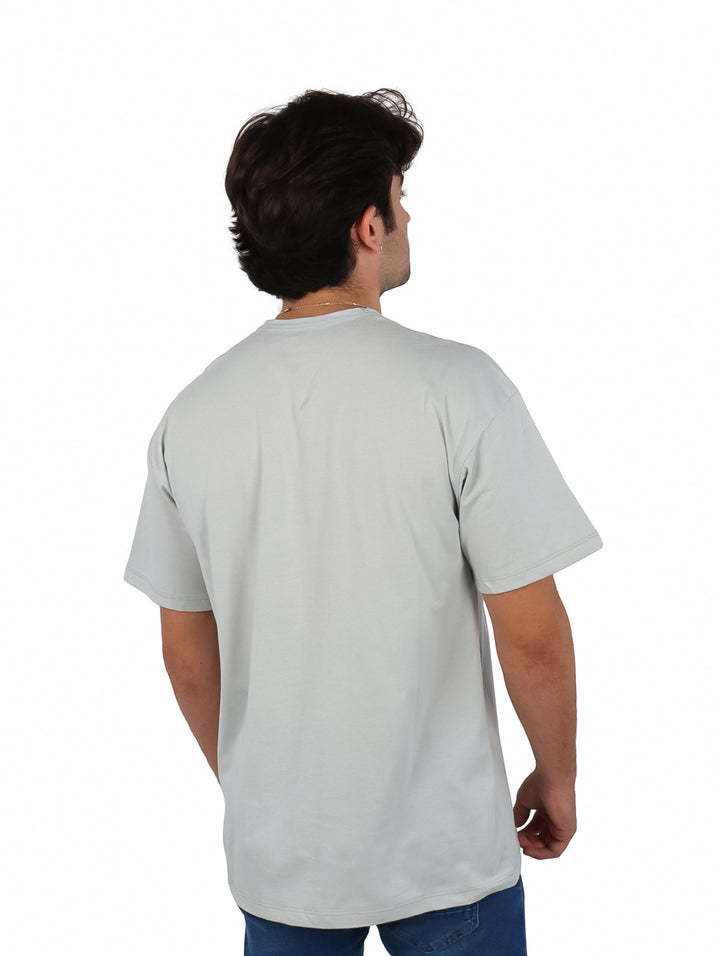 Hombre vistiendo playera oversize color gris de manga corta y cuello redondo con texto pequeño en el pecho.