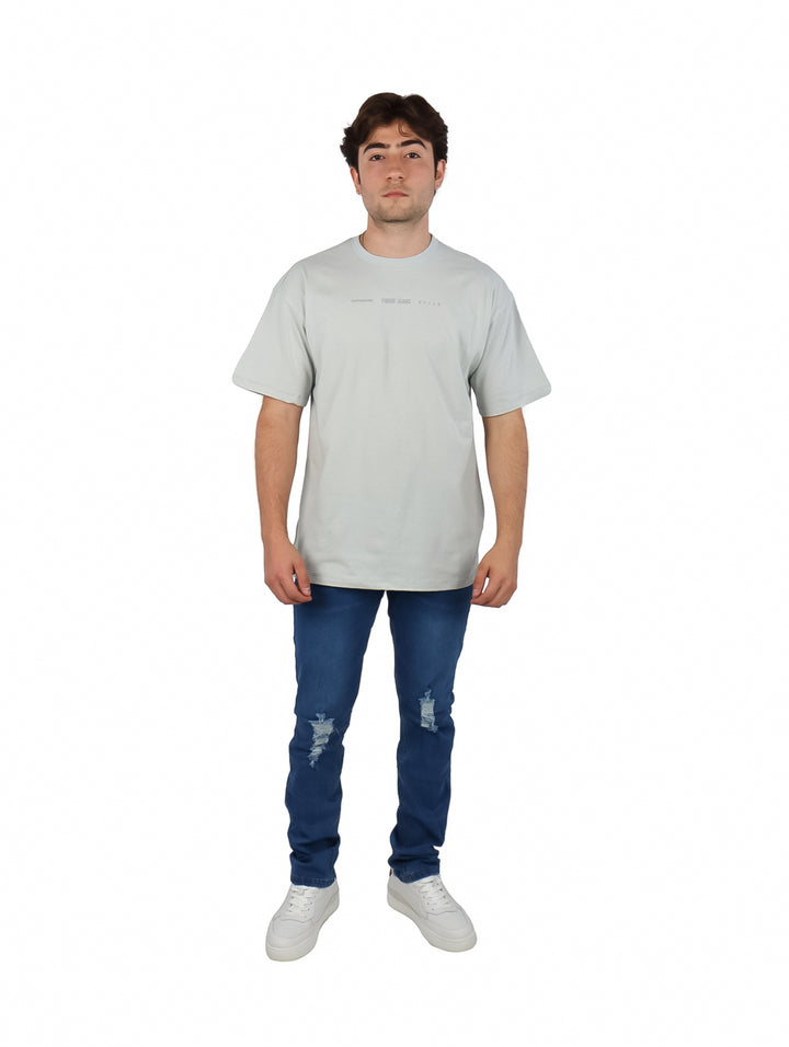 Hombre vistiendo playera oversize color gris de manga corta y cuello redondo con texto pequeño en el pecho.