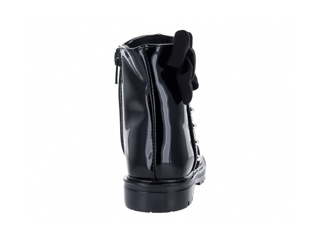 Bota de charol negro con moño decorativo y detalles metálicos.