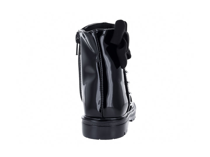 Bota de charol negro con moño decorativo y detalles metálicos.