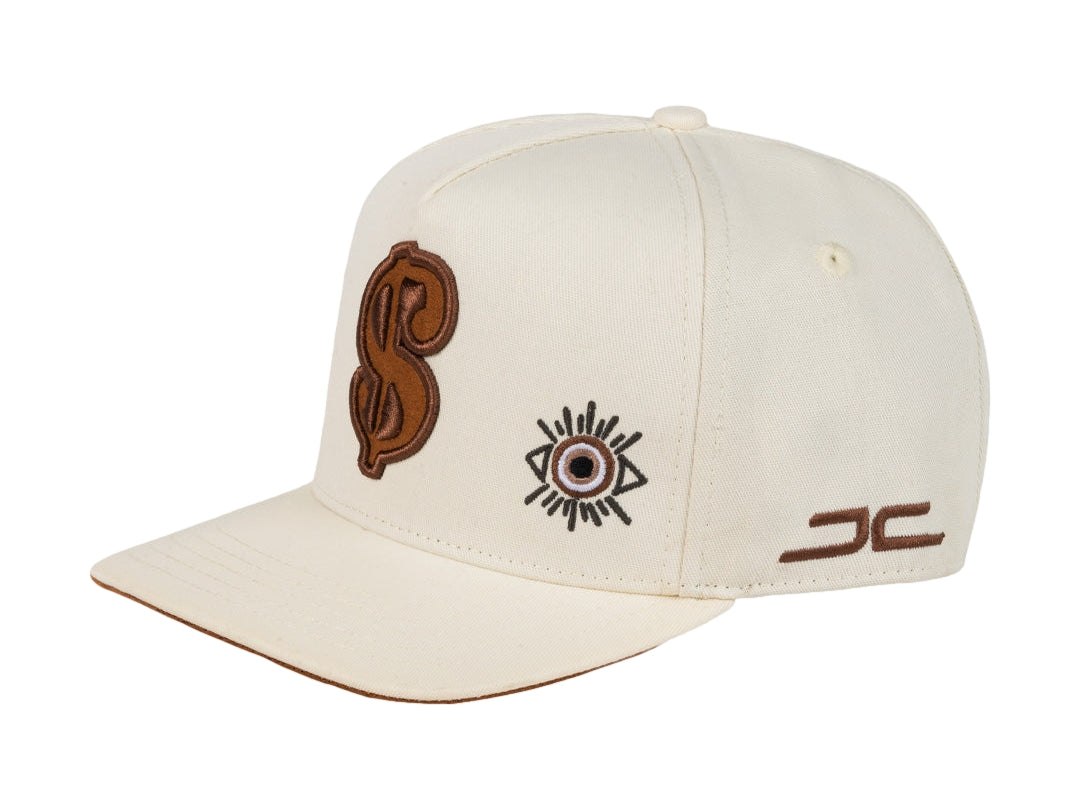Gorra snapback color beige con bordados en marrón, incluyendo un símbolo de dólar y un ojo.