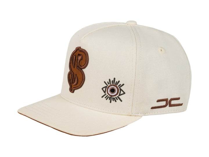 Gorra snapback color beige con bordados en marrón, incluyendo un símbolo de dólar y un ojo.
