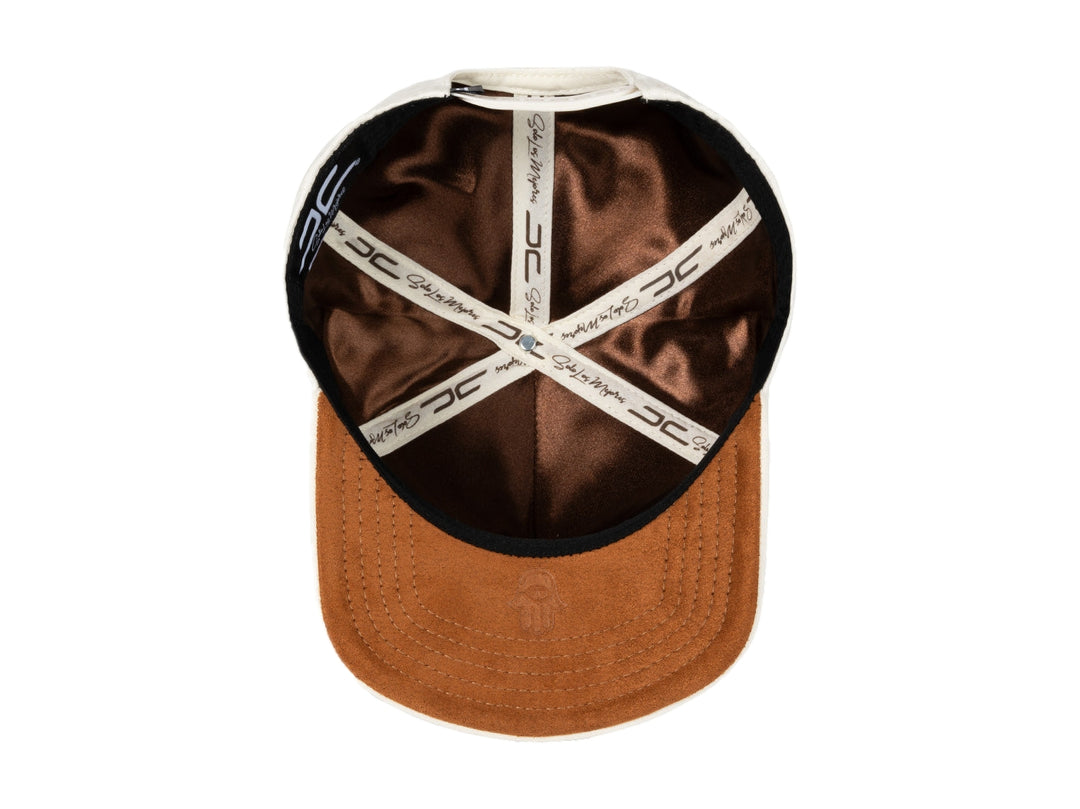 Gorra snapback color beige con bordados en marrón, incluyendo un símbolo de dólar y un ojo.