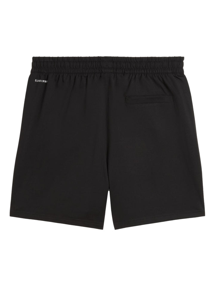 Hombre vistiendo shorts deportivos Puma color negro con logotipo blanco lateral.