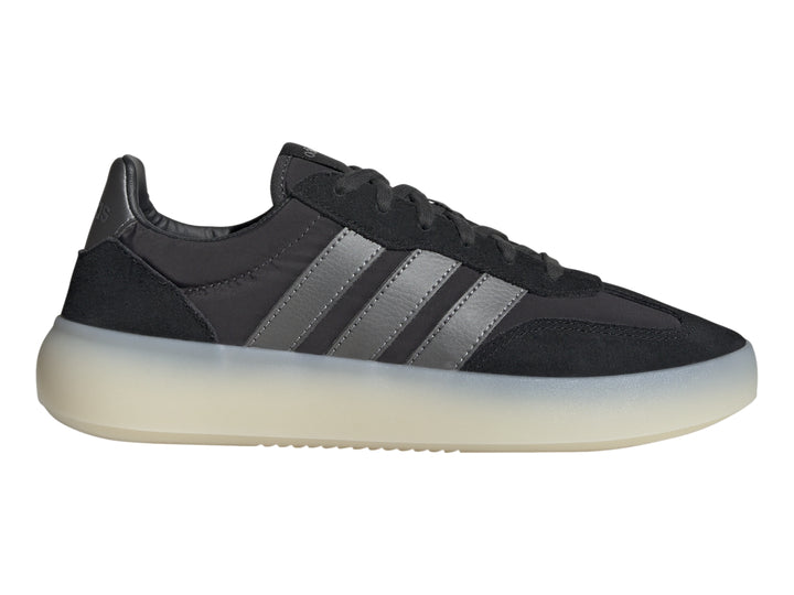 Tenis Adidas negros con tres franjas grises y suela gruesa de color blanco translúcido.