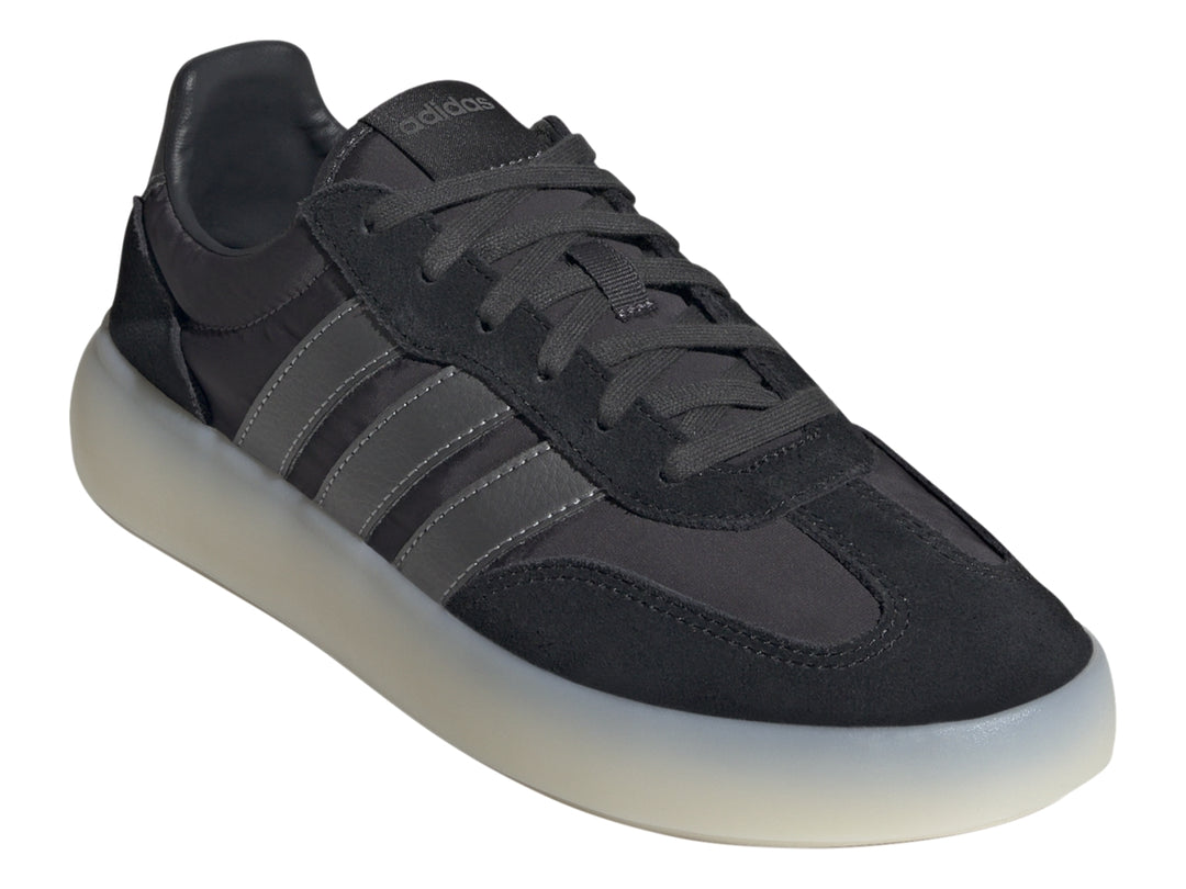 Tenis Adidas negros con tres franjas grises y suela gruesa de color blanco translúcido.