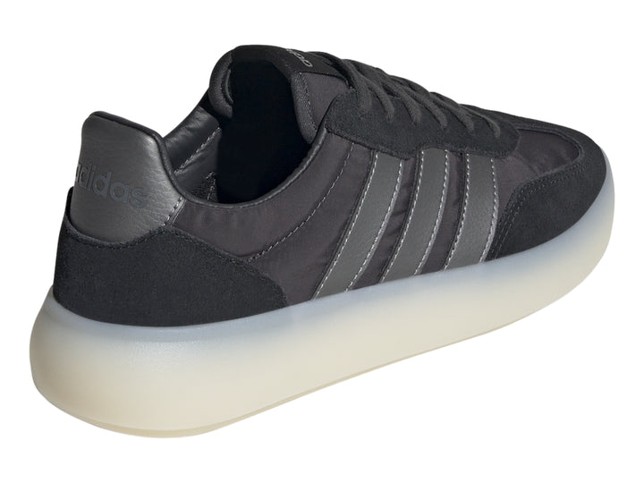 Tenis Adidas negros con tres franjas grises y suela gruesa de color blanco translúcido.