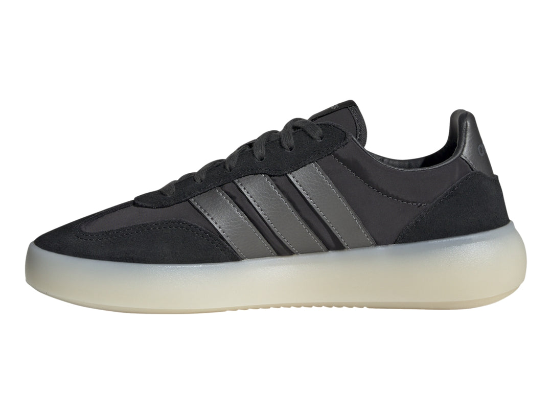 Tenis Adidas negros con tres franjas grises y suela gruesa de color blanco translúcido.