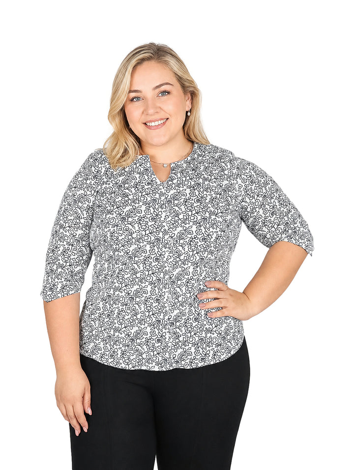 Mujer vistiendo blusa blanca con estampado floral marino de manga corta y pantalones negros.