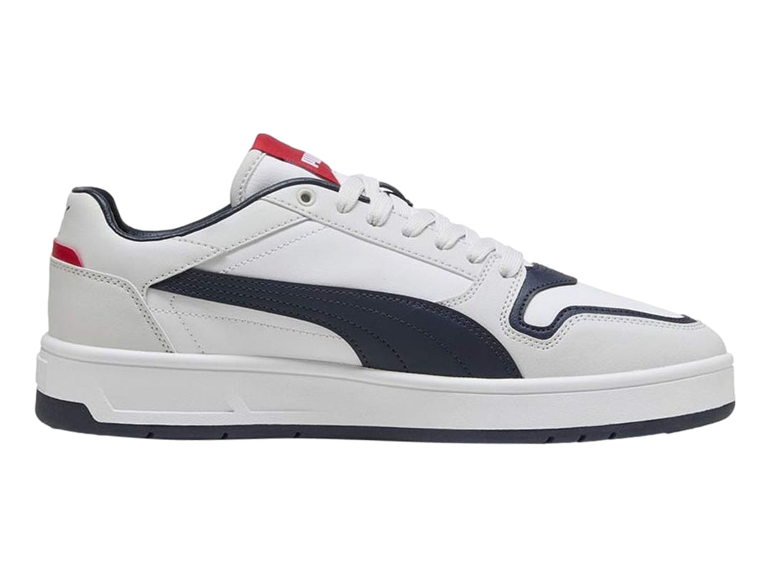 Tenis PUMA blancos con franja y suela azul marino y detalles rojos, vista lateral.