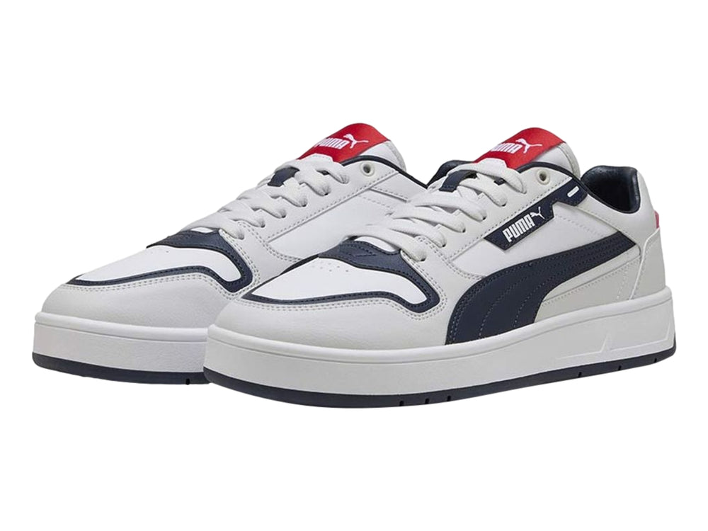 Tenis PUMA blancos con franja y suela azul marino y detalles rojos, vista lateral.