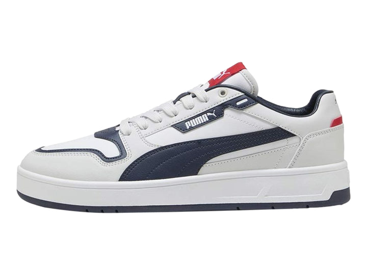 Tenis PUMA blancos con franja y suela azul marino y detalles rojos, vista lateral.