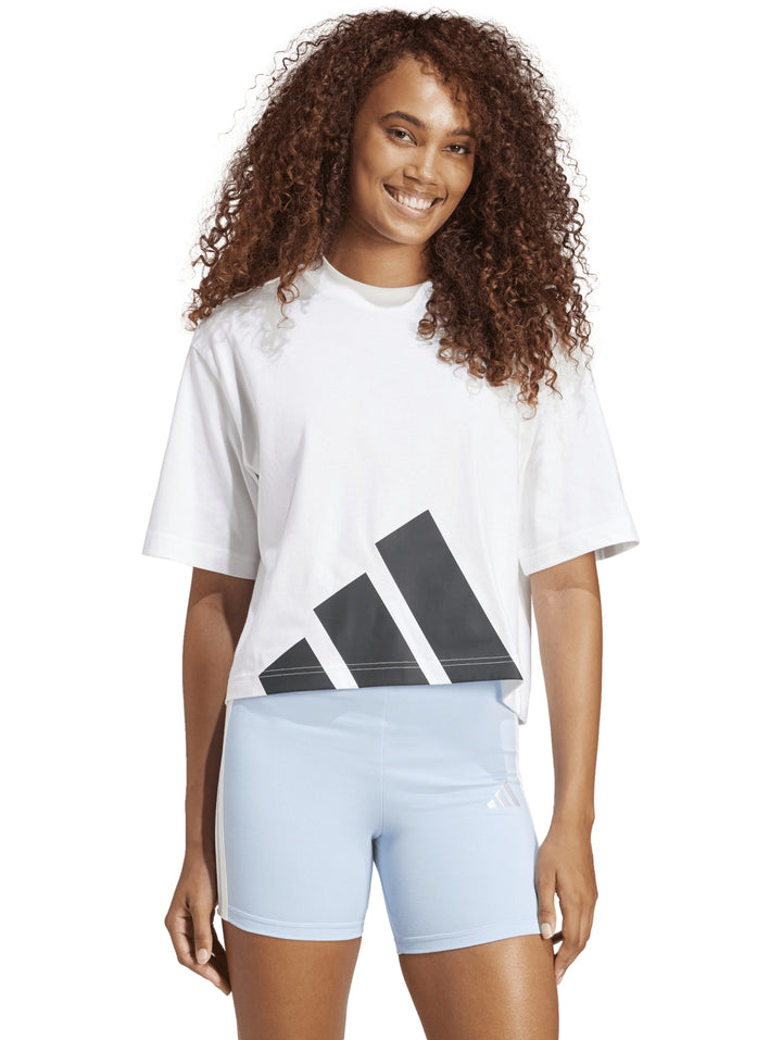 Mujer vistiendo playera blanca Adidas de corte boyfriend con logo grande en negro.