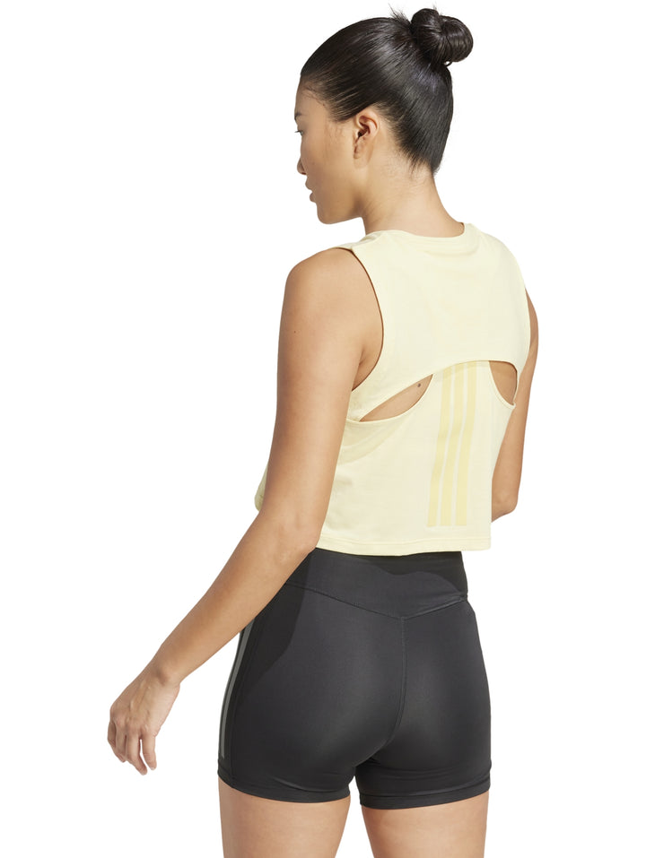 Mujer vistiendo playera sin mangas color amarillo pálido de corte boxy y shorts deportivos negros de Adidas.