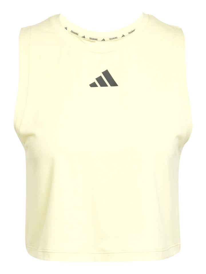 Mujer vistiendo playera sin mangas color amarillo pálido de corte boxy y shorts deportivos negros de Adidas.