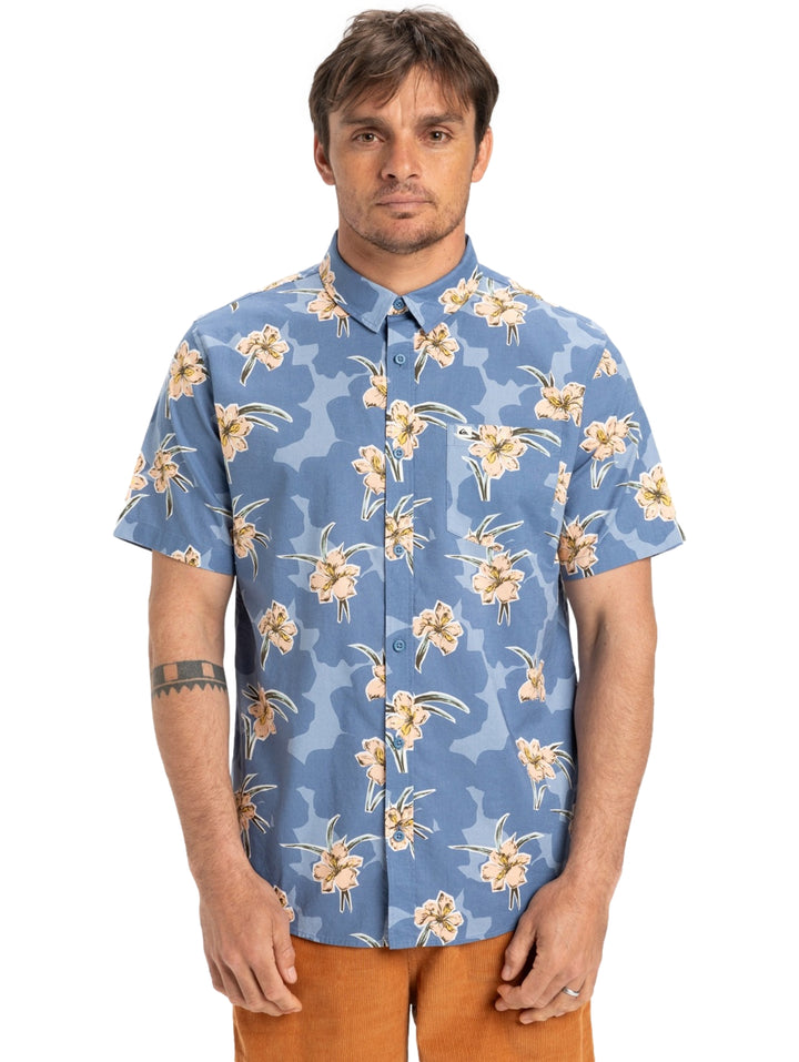 Hombre vistiendo camisa de manga corta azul con estampado floral en tonos crema.
