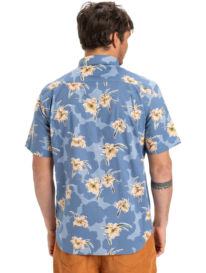 Hombre vistiendo camisa de manga corta azul con estampado floral en tonos crema.