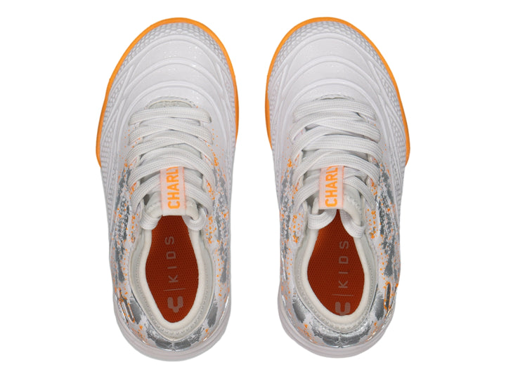 Calzado de fútbol Charly en color blanco con suela naranja y detalles decorativos plateados.