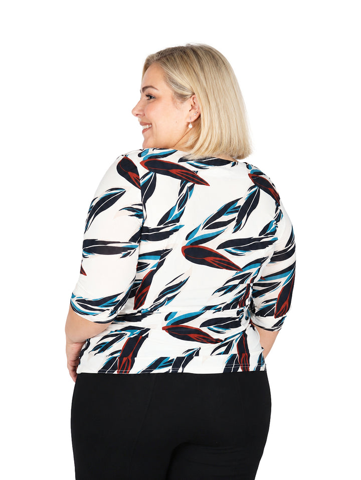 Mujer vistiendo blusa blanca con estampado de hojas en azul y rojo, de manga corta.