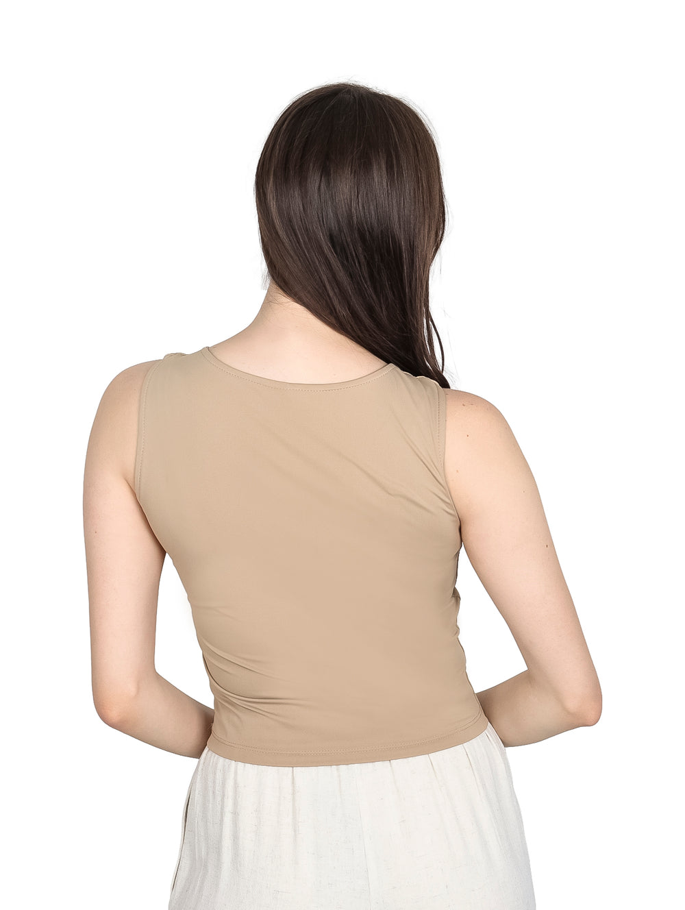 Mujer modelando una blusa sin mangas de color kaki y pantalones blancos.