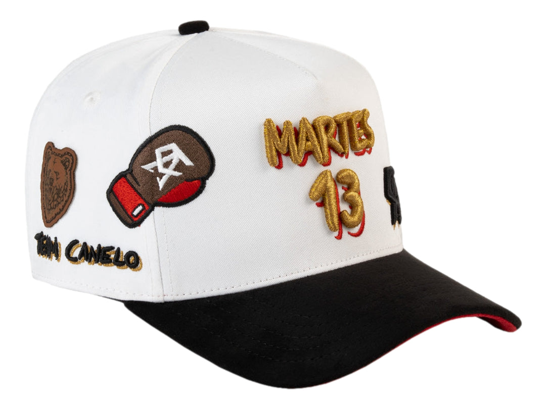 Gorra JC Hats blanca con visera negra y detalles bordados en dorado, negro y rojo.