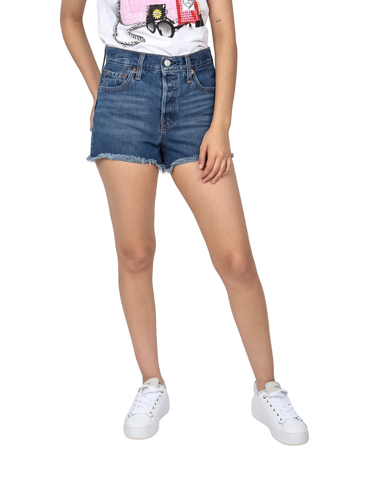 Mujer vistiendo shorts de mezclilla azul con bordes deshilachados y tenis blancos.