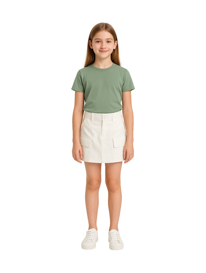 Niña vistiendo una falda blanca corta con bolsillos frontales y camiseta verde.