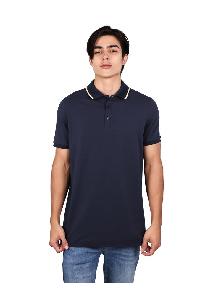 Hombre vistiendo una playera polo de color marino con detalle en el cuello y pantalones mezclilla azules.